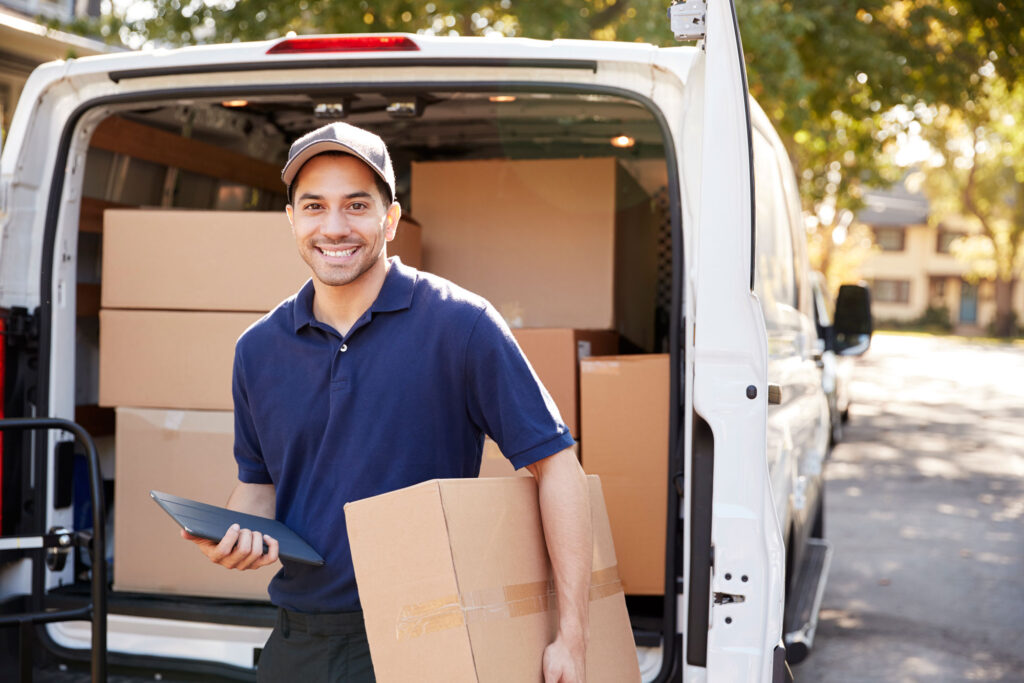 A delivery Drive standing smiling in-front of his van with boxes in the background