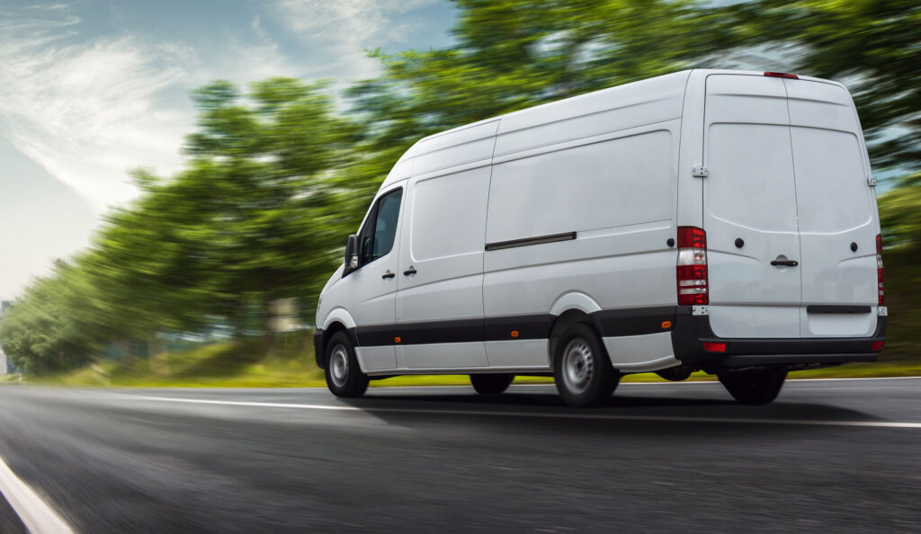 White Delivery van traveling down a country road to a city in the distance